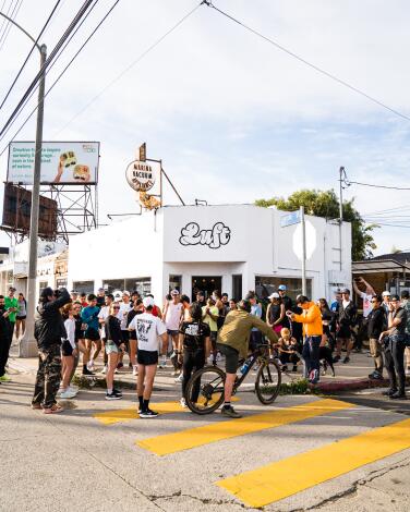 A group of bike riders in the street outside a low white building with a sign that says "Luft"