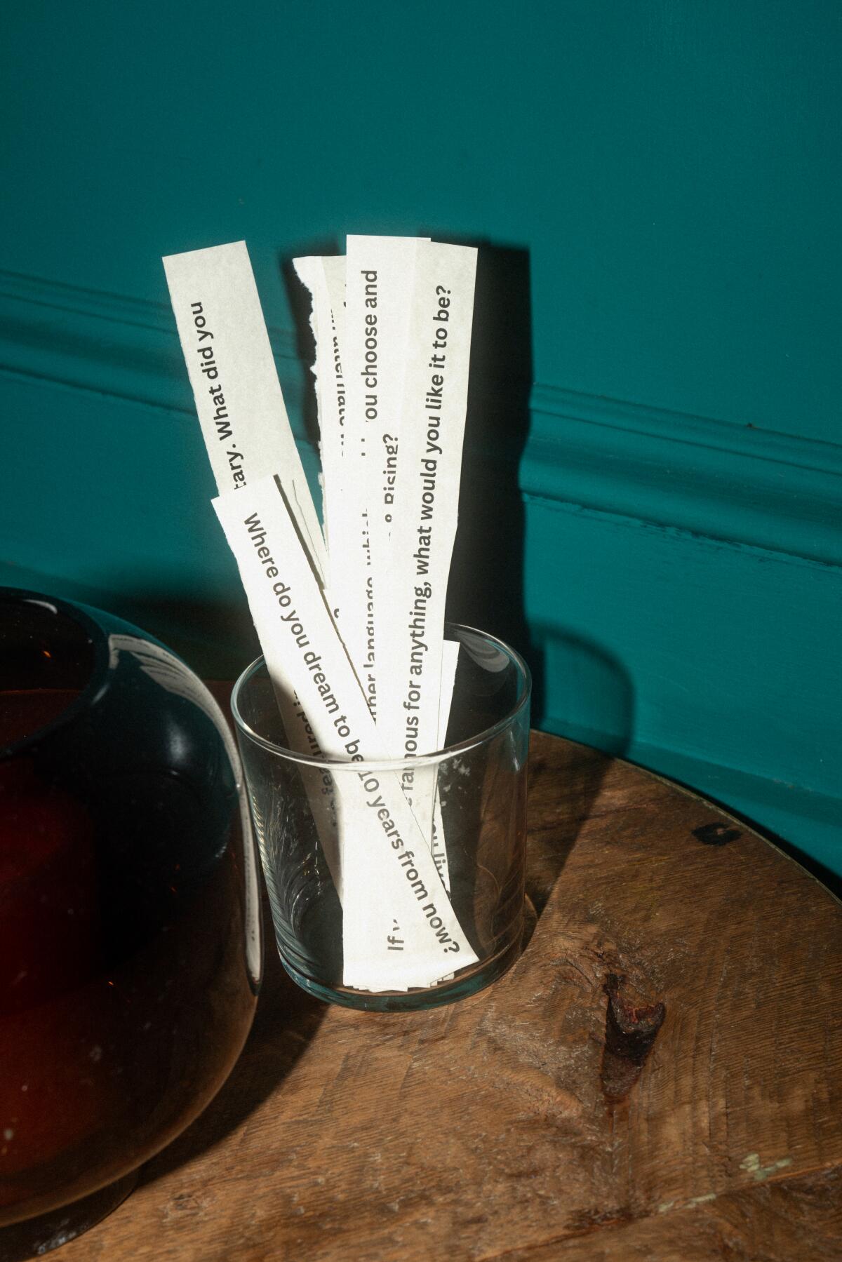 Pieces of paper with sentences typed on them stand in a glass on a table
