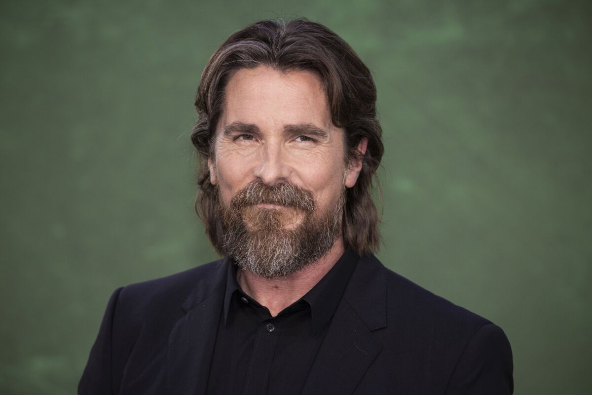 Christian Bale with long hair against a dark green backdrop