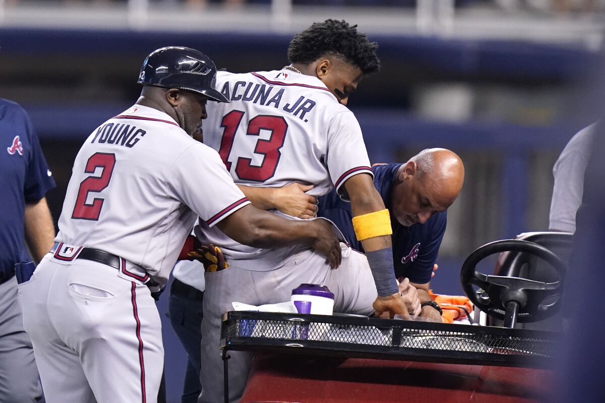 Atlanta Braves right fielder Ronald Acuna Jr., center, is helped onto a medical cart after trying to make a catch on an inside-the-park home run hit by Miami Marlins' Jazz Chisholm Jr. during the fifth inning of a baseball game, Saturday, July 10, 2021, in Miami. (AP Photo/Lynne Sladky)