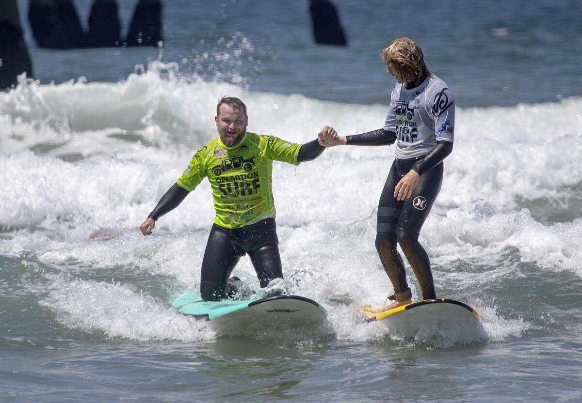 Marine Sgt. David Mahula, left, whose leg was amputated, gets a hand from volunteer Max Seirson while surfing.