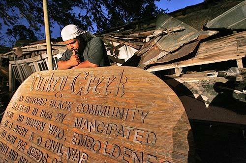 Derrick Evans, in front of his destroyed home in Turkey Creek, a Reconstruction-era black settlement in Gulfport, Miss. Evans salvaged the sign after Hurricane Katrina tossed it off the posts in front of his home. Most of the area's 300-400 residents descend from the original homesteaders--emancipated black landowners.