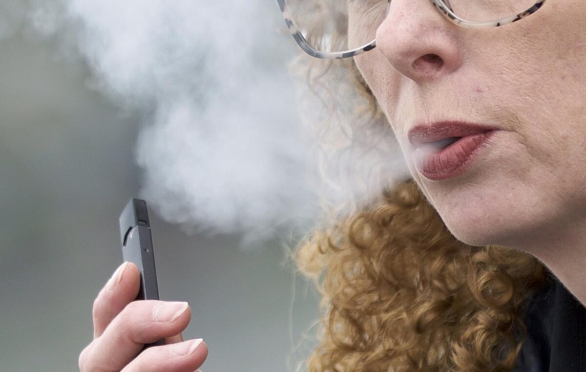 A woman exhales while vaping from a Juul pen e-cigarette in Vancouver, Wash.