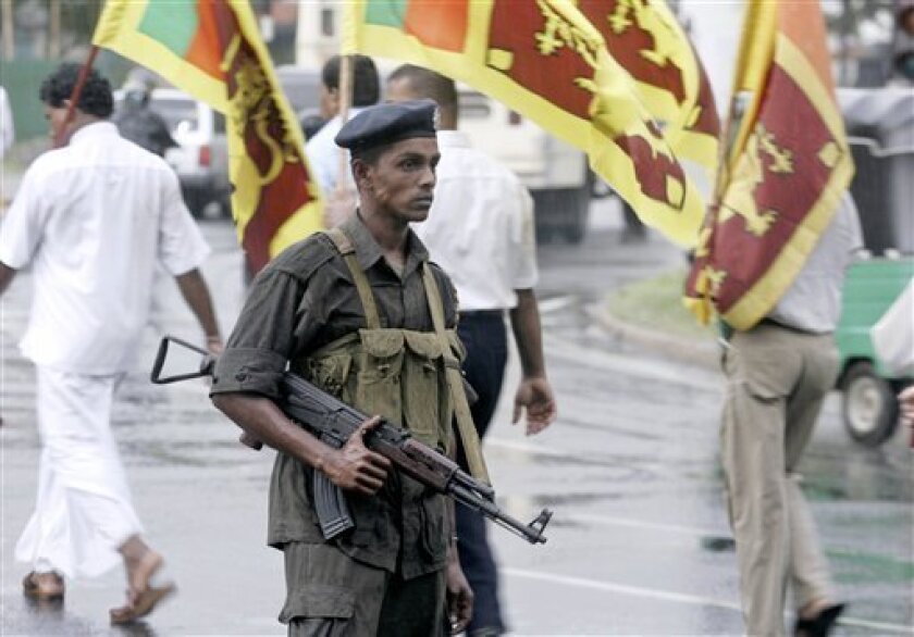 A Sri Lankan soldier stands guard as members of Sri Lanka's hard line nationalist party Jathika Hela Urumaya, also known as National Heritage, parade in streets carrying Sri Lankan national flags during a march in honor of the Sri Lankan defense forces in Colombo, Sri Lanka, Wednesday, Nov. 19, 2008. Sri Lankan air force jets bombed a rebel training camp in the north as ground forces waged new battles with Tamil Tiger rebels across the front lines, the military said Wednesday.(AP Photo/Eranga Jayawardena)