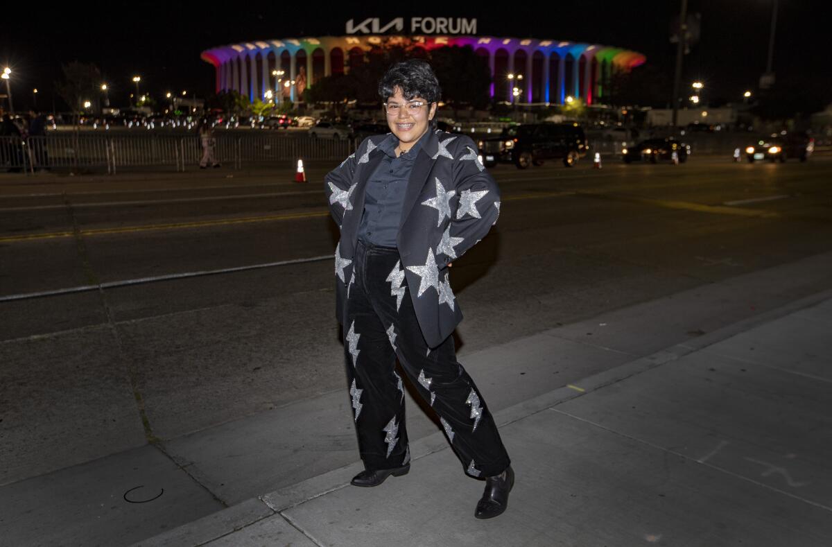 A young music fan poses outside of the Kia Forum, which is lit up in rainbow colors