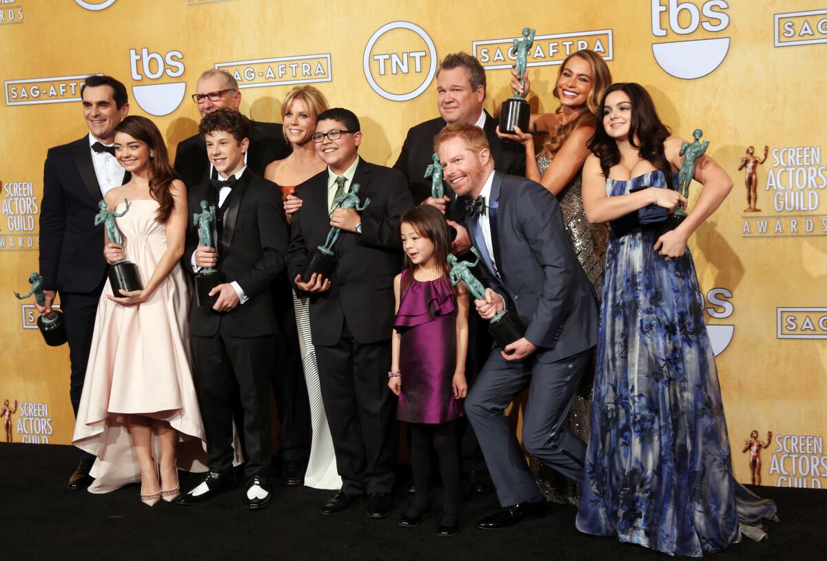 The cast of sitcom "Modern Family" huddles and poses together while holding SAG award statuettes