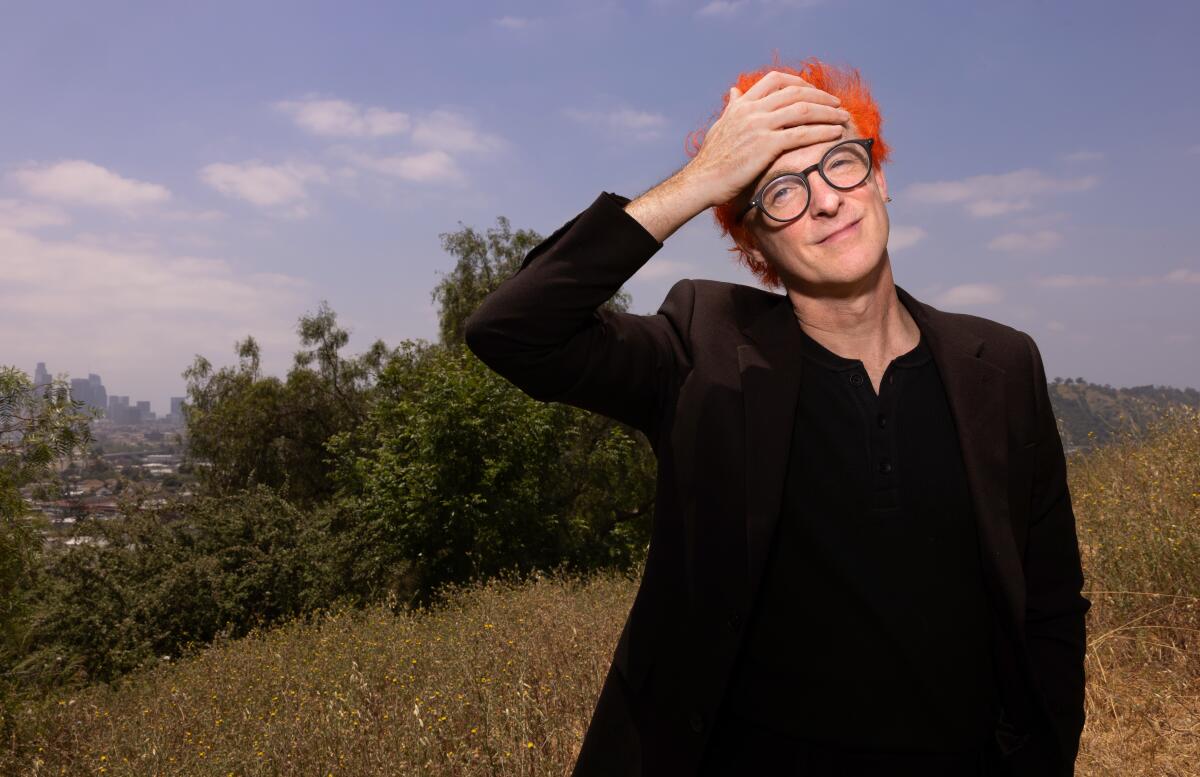 Man with bright orange hair and glasses posing in a field