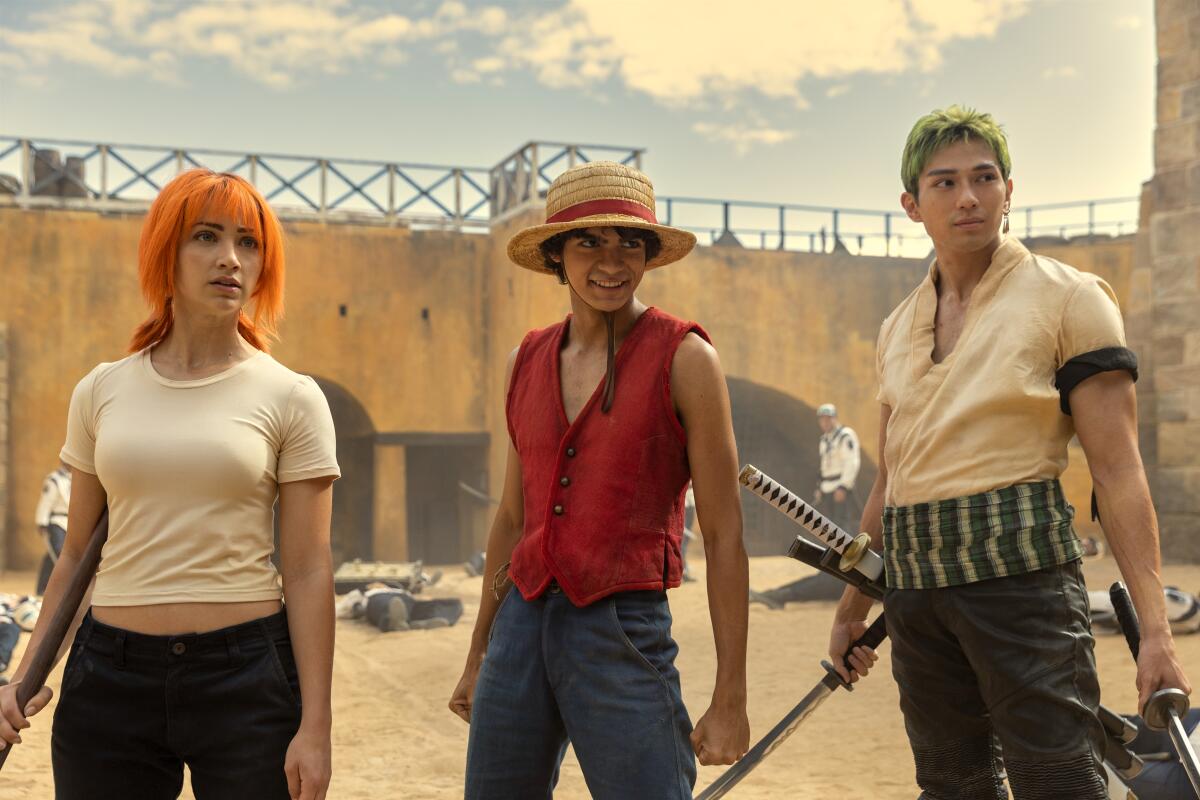 Nami, Monkey D. Luffy and Roronoa Zoro stand side by side in the courtyard of a building.