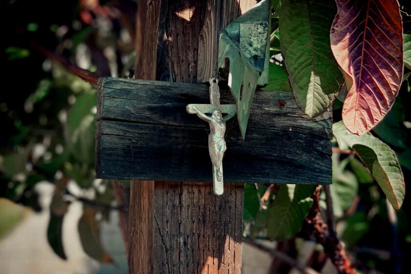 A small silver crucifix is seen nailed to a wooden post in the backyard of Alex Espinoza.