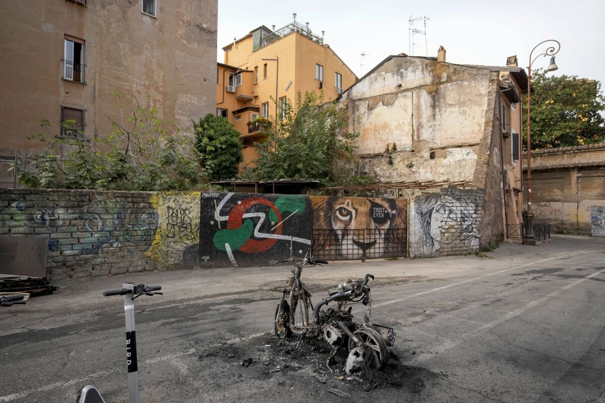 A burnt scooter is abandoned in a parking lot of Trastevere's neighborhood of Rome, Wednesday, Sept. 15, 2021. Romans are fed up with piles of uncollected garbage, subway stations closed down for months for repairs and weeds growing so tall, they reached the door handles of parked cars. (AP Photo/Andrew Medichini)
