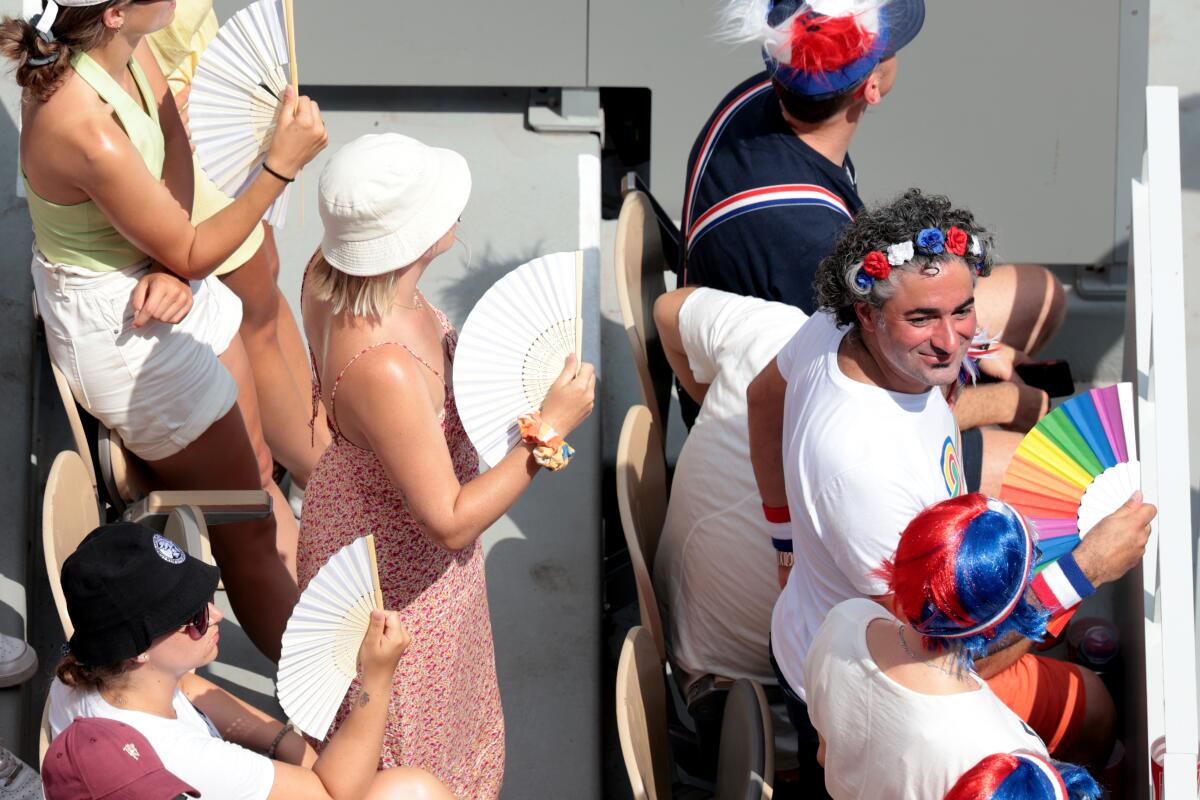 Spectators use fans to stay cool while watching Olympic tennis at Roland Garros.