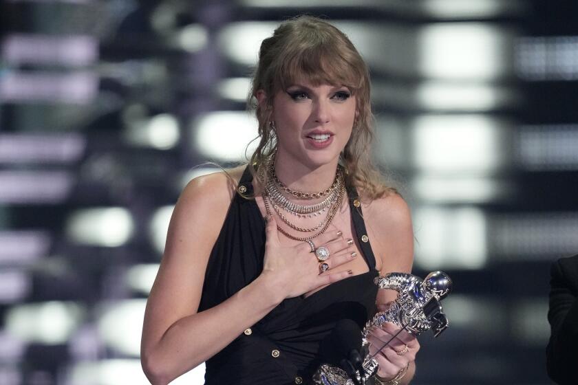 Taylor swift holds a trophy with one hand and places the other on her chest while accepting an award at an awards show