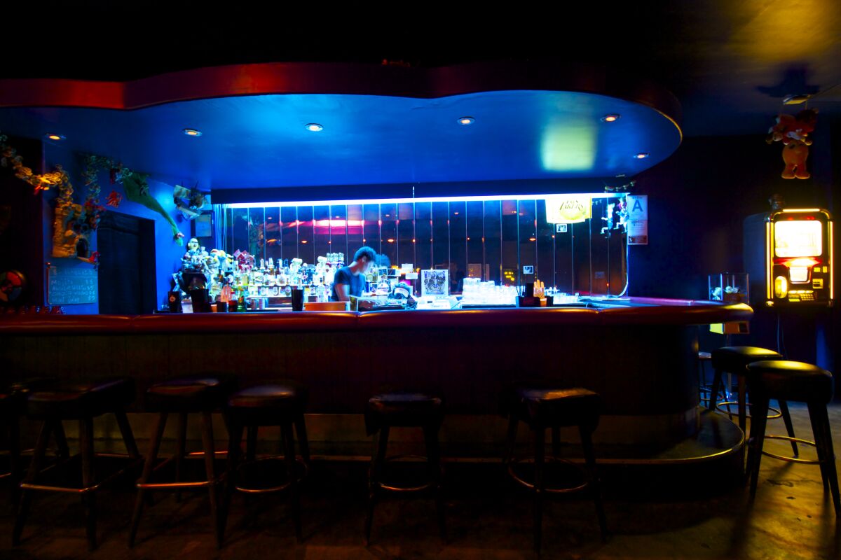 A bartender works at a blue-lit bar in a dark room.