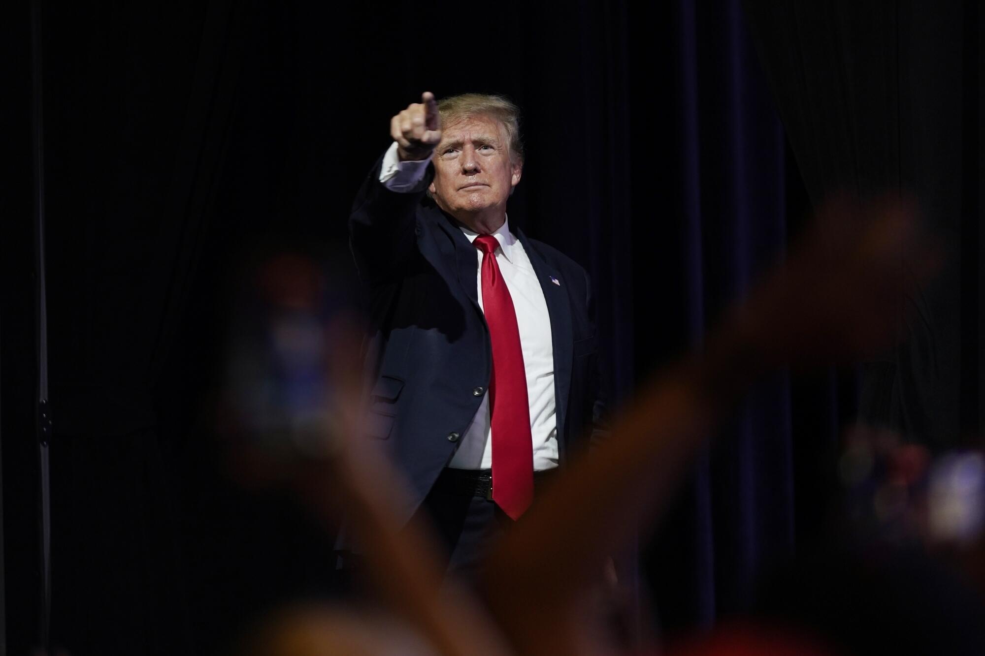 Donald Trump, framed by blurred heads in a crowd, standing and pointing