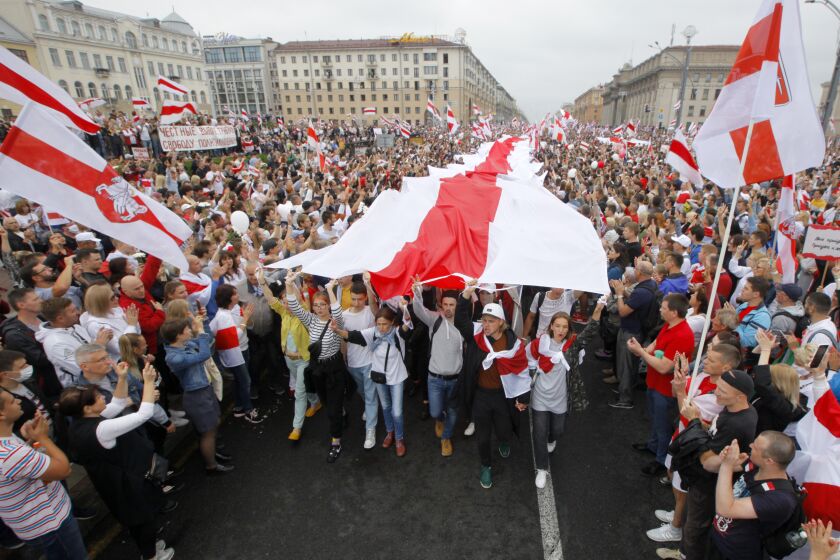 Demonstrators carry historical flags of Belarus as thousands gather for a protest at the Independence square in Minsk, Belarus, Sunday, Aug. 23, 2020. Demonstrators are taking to the streets of the capital and other cities, keeping up their push for the resignation of the nation's authoritarian leader. President Alexander Lukashenko has extended his 26-year rule in a vote the opposition saw as rigged. (AP Photo/Dmitri Lovetsky)