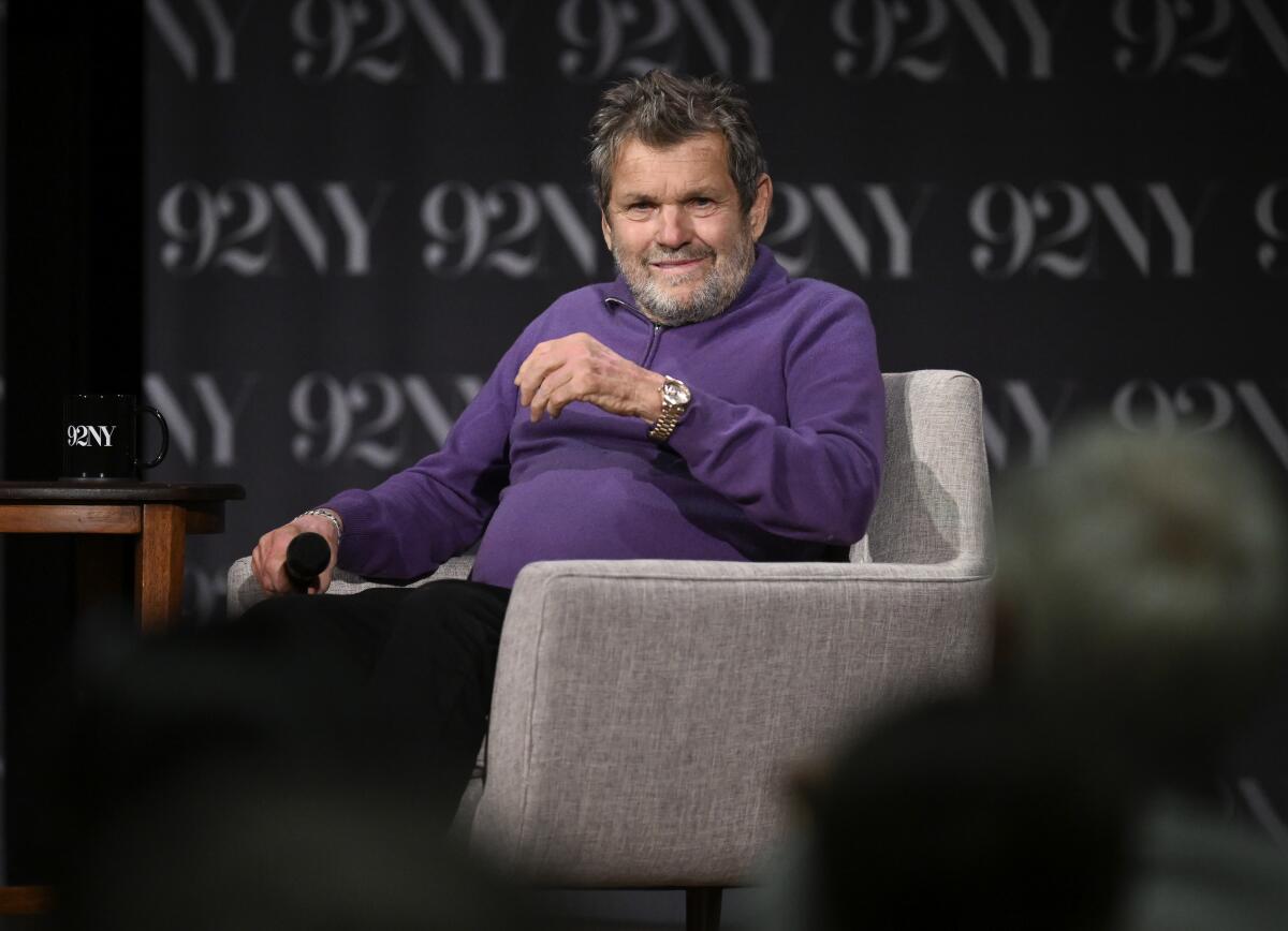 Jann Wenner sits in a chair holding a microphone.
