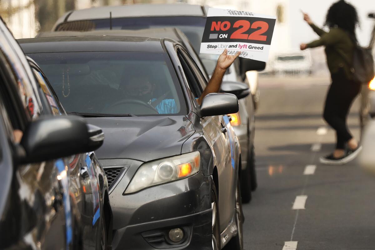 A ride-hail driver holds a sign that says No on 22.