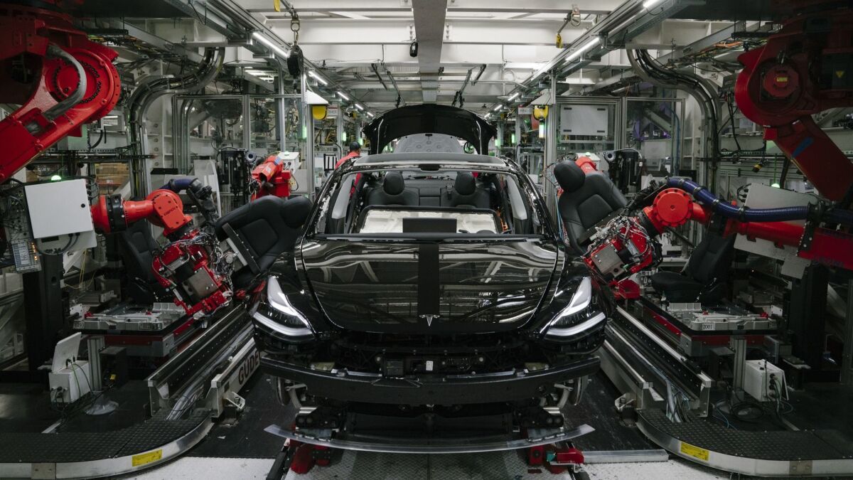 Robotics arms install the front seats of a Tesla Model 3 at the Tesla factory in Fremont, Calif., on July 26.