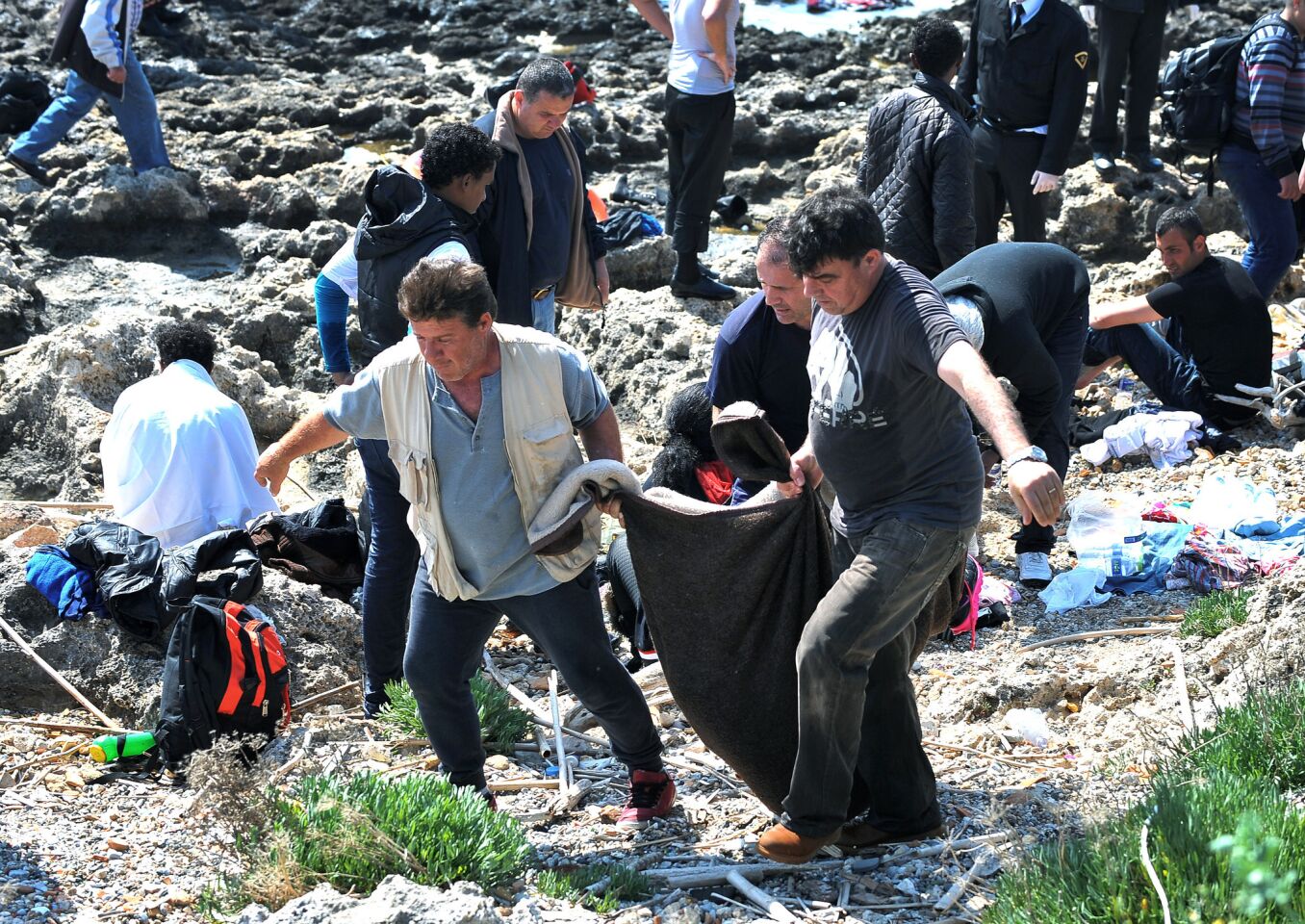 Men carry a dead body inside a blanket on the shore in the eastern Aegean island of Rhodes, Greece. Authorities said that at least three people have died, including a child, after a wooden boat carrying many migrants ran aground off the island of Rhodes.