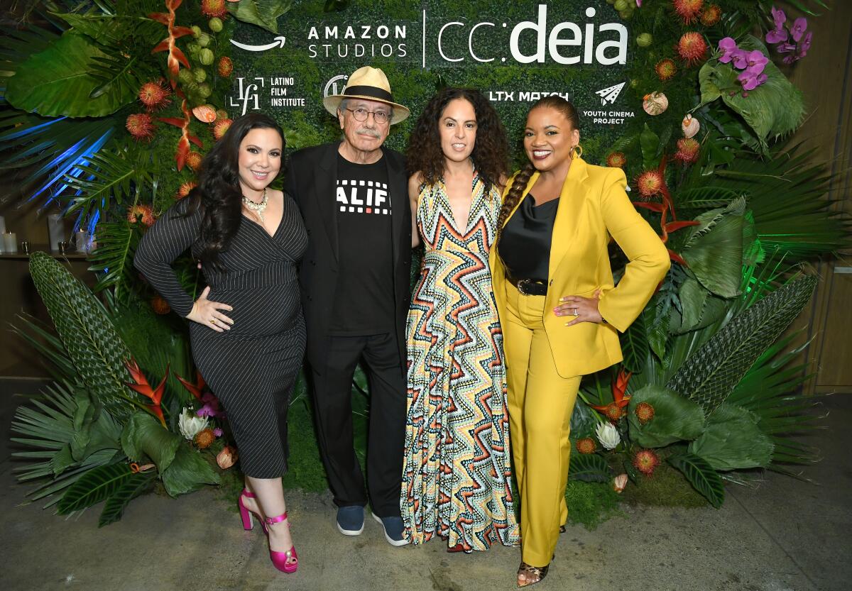 Three women and a man pose for photos on a red carpe 