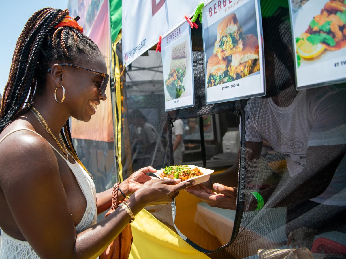 A woman receives a plate of food from a person inside an Ethiopian food truck 