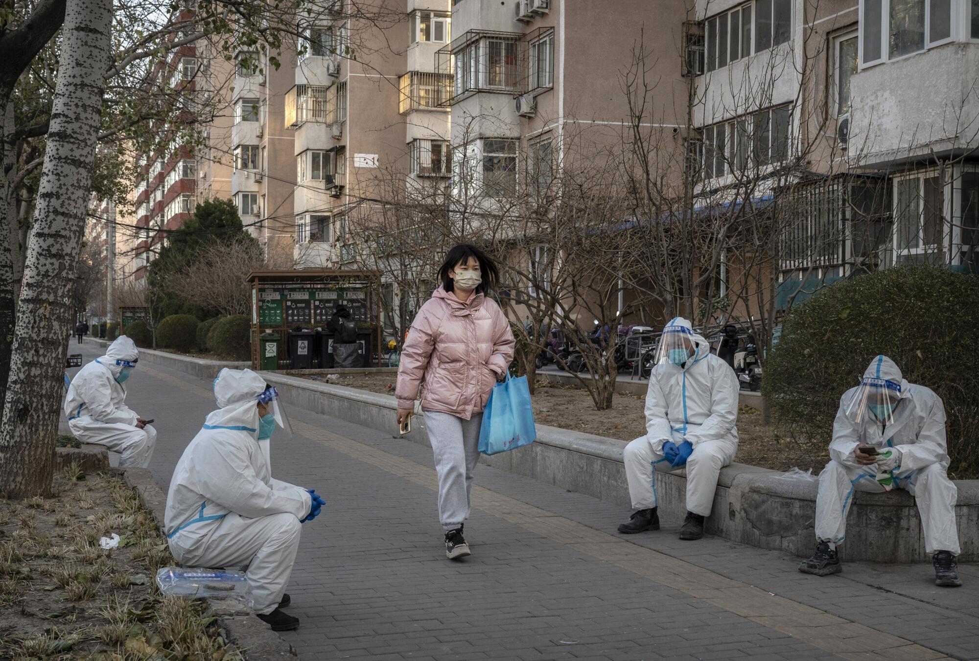 A pedestrian walks by epidemic control workers who work in sanitation wearing PPE 