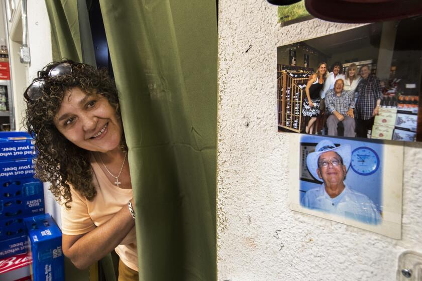 TRINIDAD, COLORADO-JULY 16, 2019: Carol Cometto, manager of the Tire Shop Wine and Spirits in Trinidad, Colorado, stands next to a photograph of Dr. Stanley Biber, lower right, taped to the wall inside the office. Cometto, who was delivered by Dr. Biber, said that she looks at this photograph almost every day she is at work. She called him, Òan amazing man.Ó (Mel Melcon/Los Angeles Times)