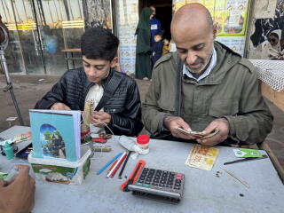 Two men sit at a table with money and repair tools.