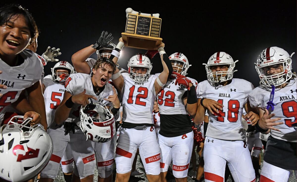 A football player holds up a trophy while flanked by other football players.