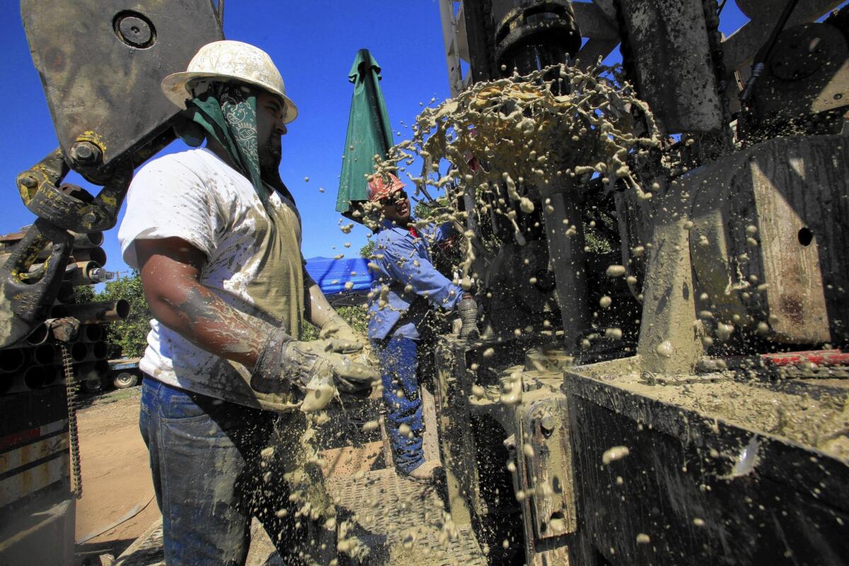 Well drilling workers Tommy Hutchinson, left, and Angel Pimentel react to a gush of muddy water as they prepare to drill deeper. Demand is so high that their employer's waiting list is a year long.