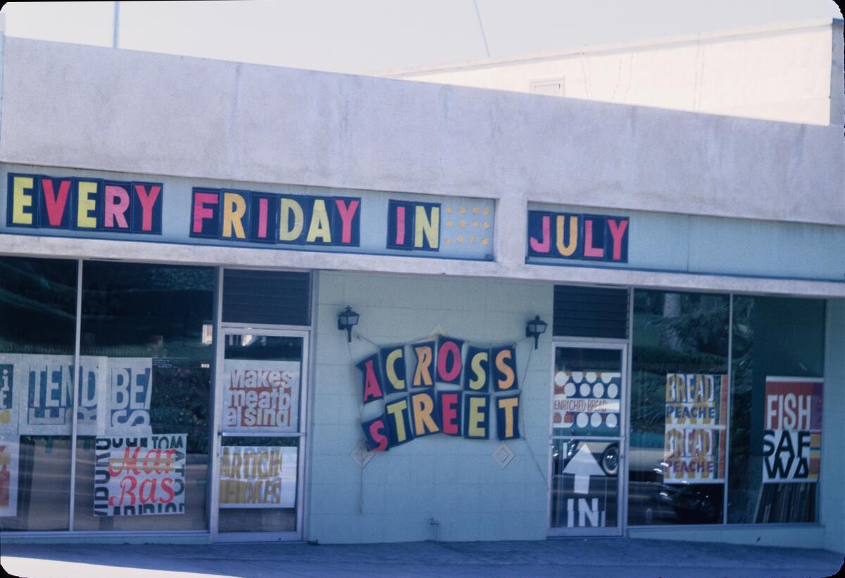 A vintage color photo shows the studio's windows covered in bright prints bearing phrases such as "makes meatball sing"