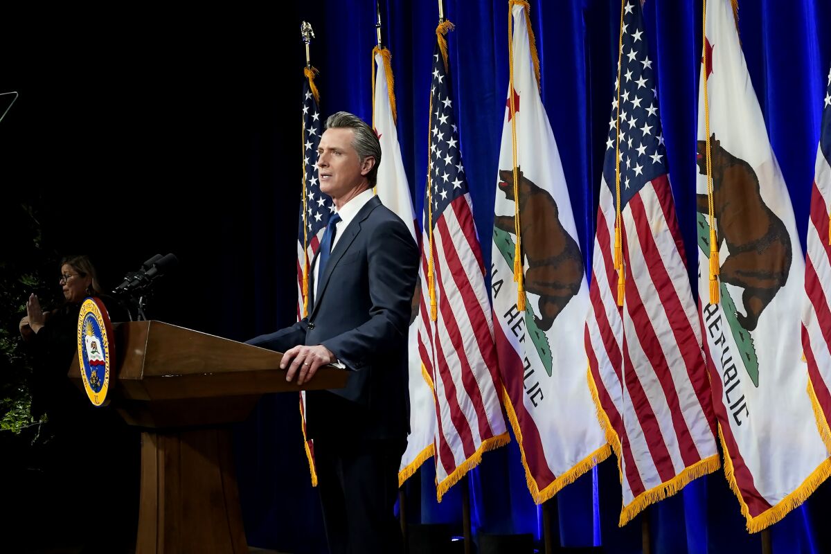 California Gov. Gavin Newsom stands at a lectern with U.S. and California flags behind him.