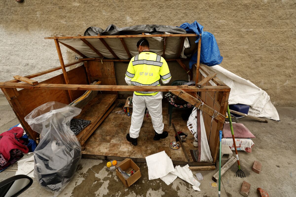 A worker in a yellow safety vest checks a makeshift wooden shelter