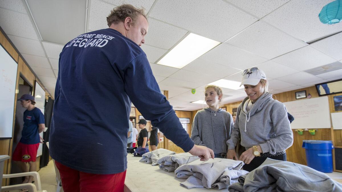 Spencer Smith, left, a Newport Beach lifeguard, helps Courtney McKenna, 11, and her mother, Marcy, choose a Junior Lifeguards sweatshirt at the Junior Guards headquarters.