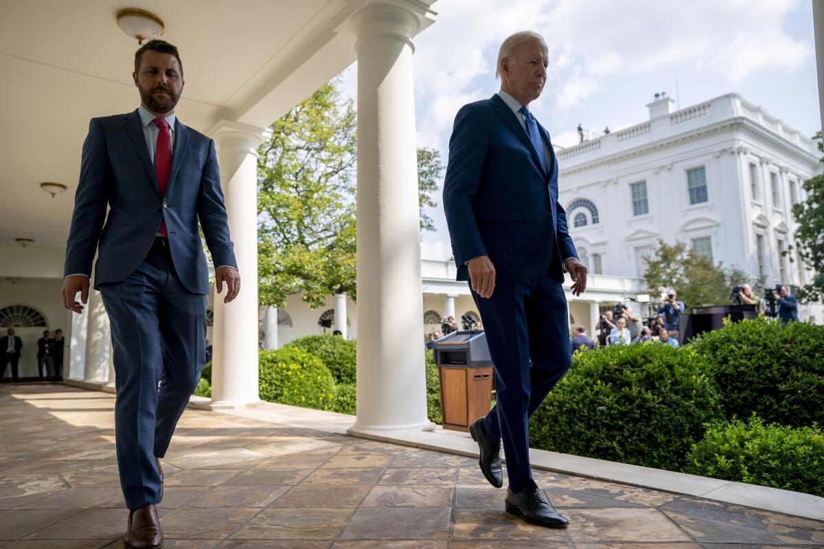 Two men in suits walk along an outside walkway