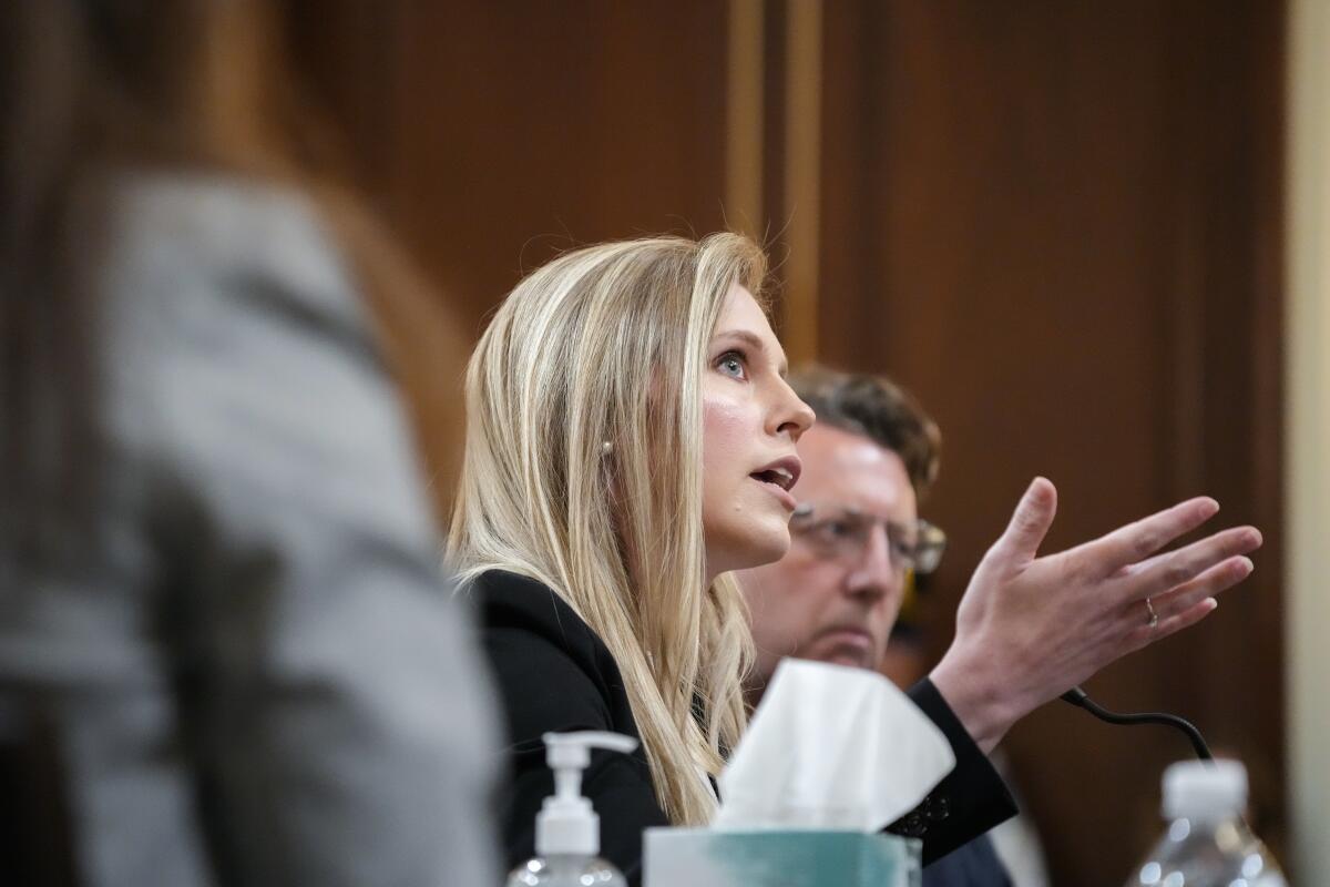 A woman with long blond hair gestures as she speaks before a microphone 