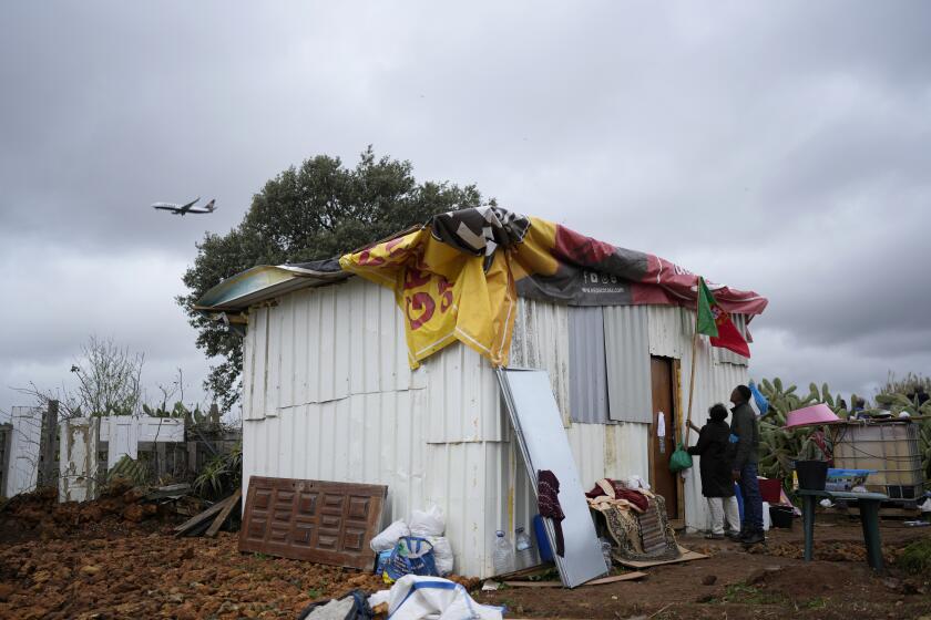 FILE Daisy and a friend attach a Portuguese flag to her makeshift house while a low-cost airline jet approaches for landing in Lisbon, in Loures, Portugal, Monday, March 6, 2023. Daisy was hoping the flag could provide some kind of protection, before the arrival of municipal workers sent to demolish the house. Seven families, mostly immigrants from Sao Tome & Principe, were evicted and had their illegal houses demolished. They had built their houses in the last couple of years when unable to pay the rising rents being asked. (AP Photo/Armando Franca, File)