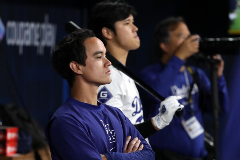 Will Ireton folds his arms while standing next to Shohei Ohtani in the Dodgers dugout 