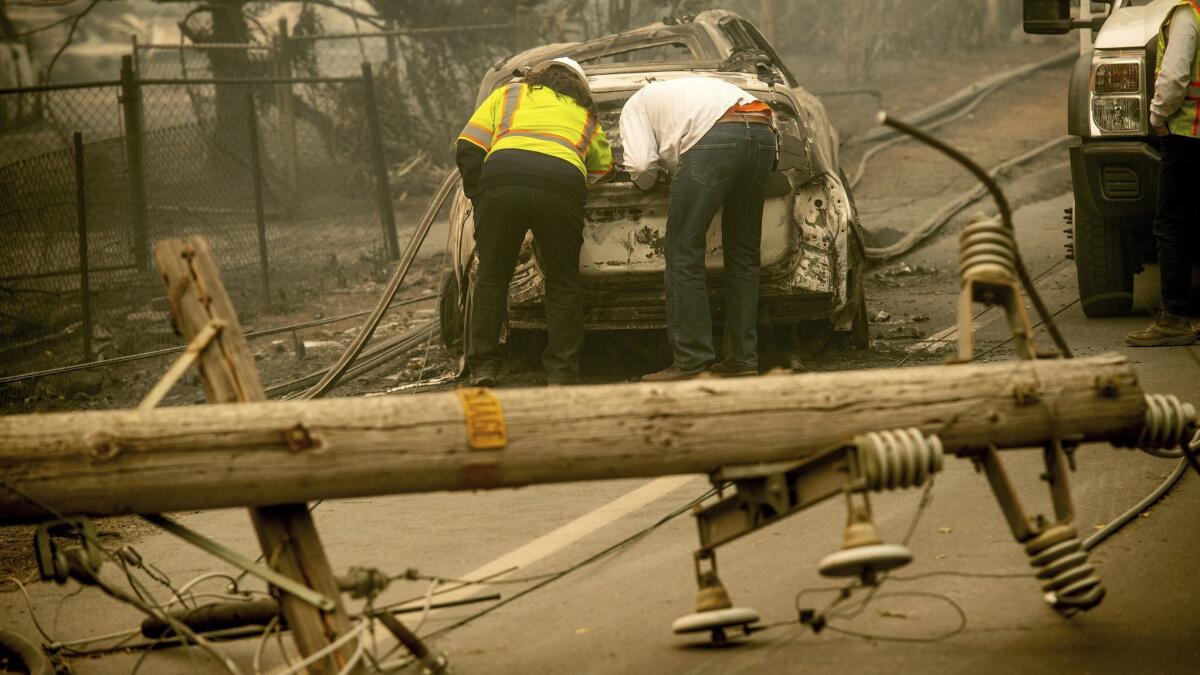 Two men look through a vehicle with a downed utility pole in the foreground after the Camp fire burned through Paradise, Calif., in November. PG&E is facing billions in potential damages because of the disaster.