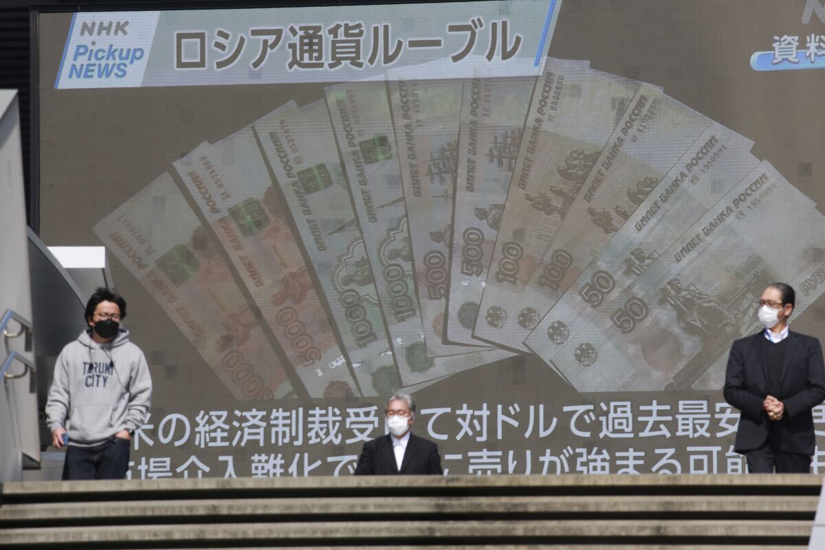 FILE - People walk in front of a huge TV screen showing banknotes of Russian ruble in Tokyo, Tuesday, March 1, 2022. Russia said Wednesday, April 6, that it made a debt payment in rubles this week, a move that may not be accepted by Russia’s foreign debtholders and could put the country on a path to a possible historic default. (AP Photo/Koji Sasahara, File)