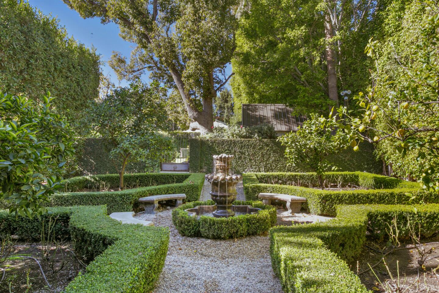 The garden has walkways and trimmed hedges and trees.