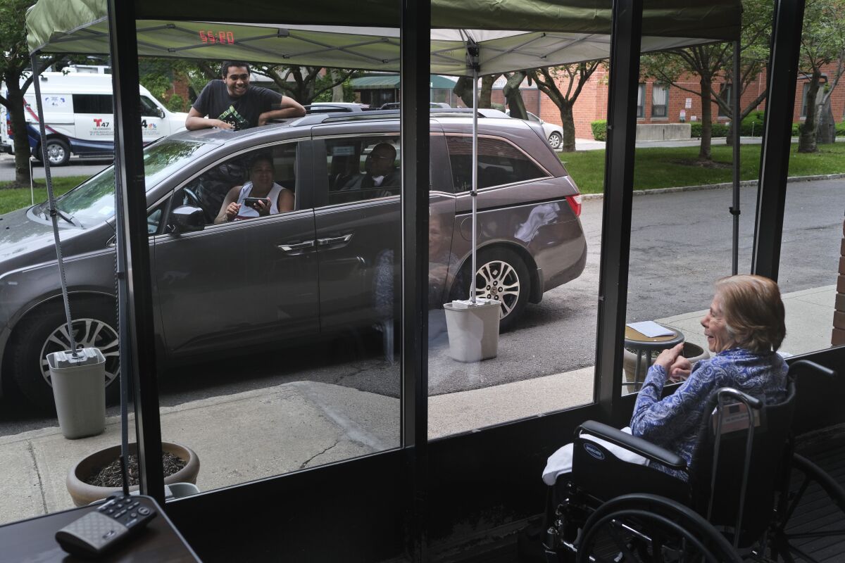 FILE - Gloria DeSoto, 92, right, visits with her family, in their car, from a window of the Hebrew Home at Riverdale, where she lives, in New York, Thursday, June 11, 2020. A focus on the elderly at the start of the nation's vaccination campaign helped protect nursing homes that were ravaged at the height of the U.S. coronavirus outbreak, but they are far from in the clear. New outbreaks, often traced to infected staff members, are still occurring in long-term care centers across the country, causing continued havoc for visitation policies. (AP Photo/Seth Wenig)
