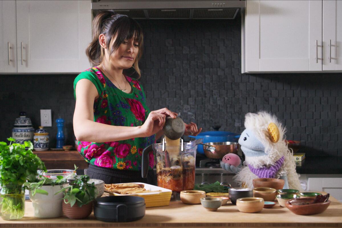 A woman shows a felt mochi and a furry puppet with waffle ears how to make mole