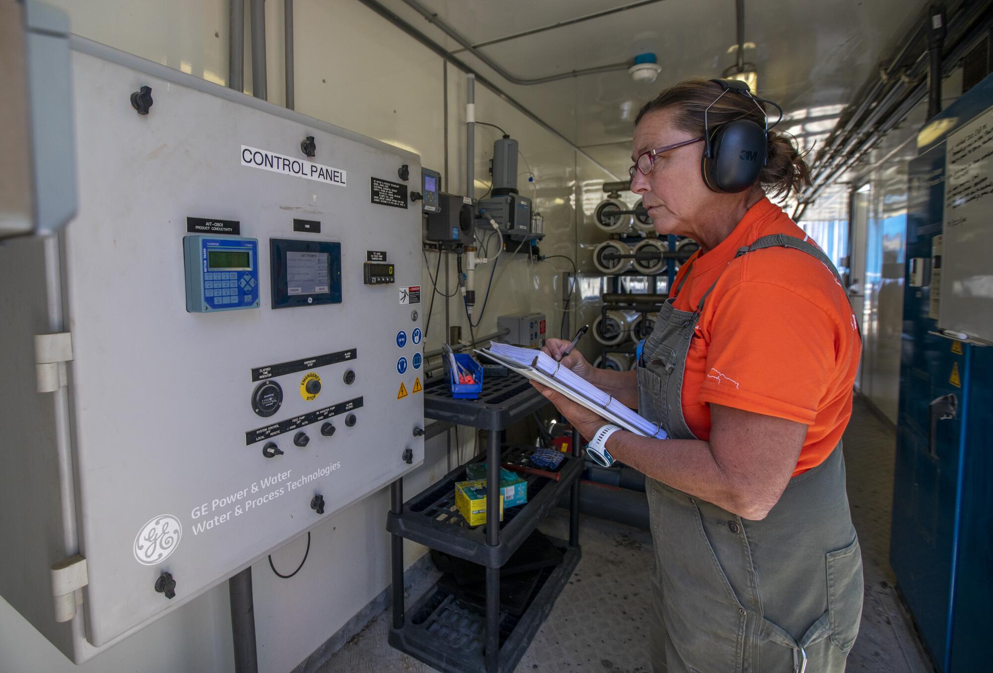 A female water and gas operator mechanic at Southern California Edison checks the numbers on a control panel 
