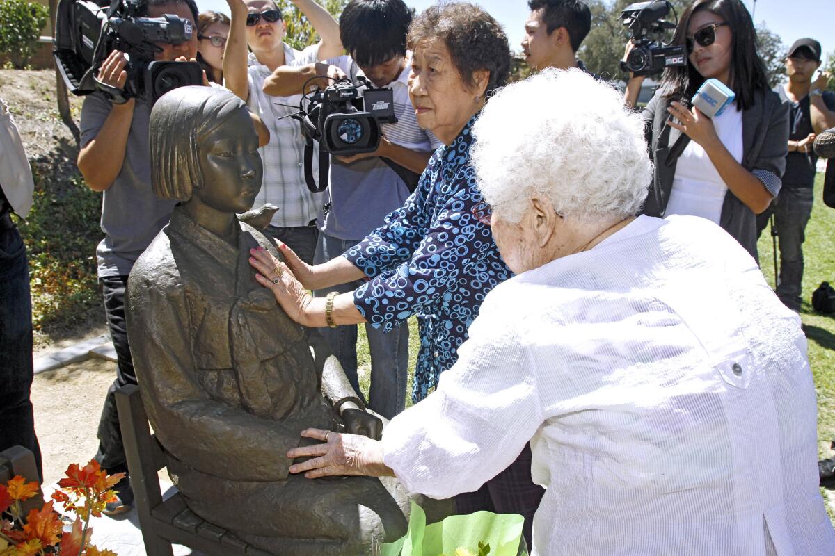 Surrounded by Korean and Japanese media, former Japanese Imperial army sex slaves Il-Chul Kang, 85, left, and Ok-Seon Lee, 87, right, caress the Peace Monument dedicated to comfort women at Central Park in Glendale on Thursday, July 24, 2014. The two Korean women were used as sex slaves during World War II by the Japanese army.