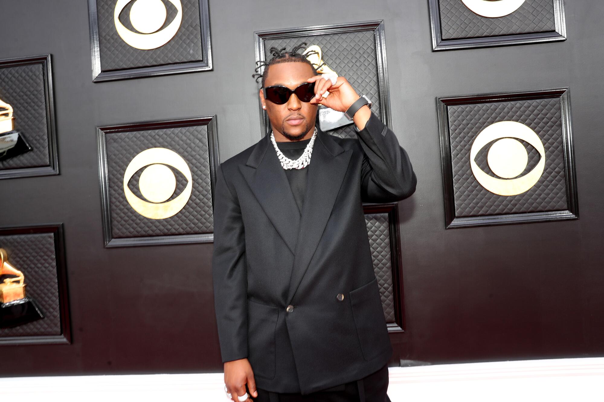 A man on the Grammys red carpet holding his glasses.