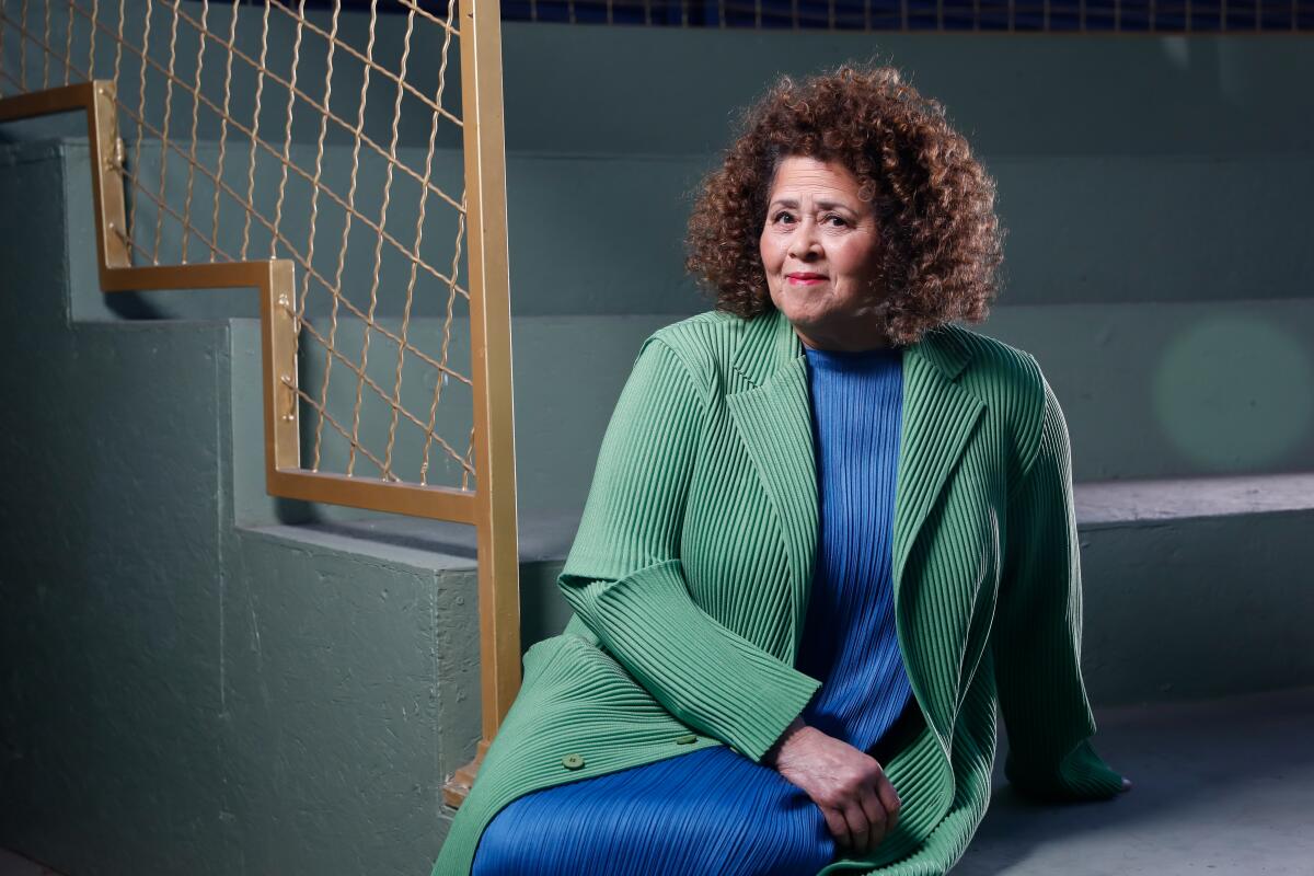 Playwright Anna Deavere Smith, in a green jacket over a blue dress, sits on stairs.