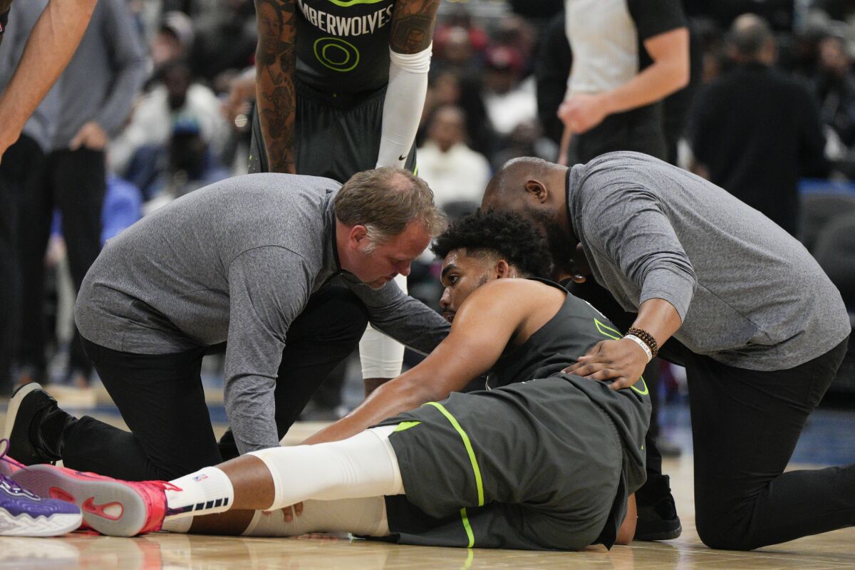 Two team staff members attend to Minnesota Timberwolves center Karl-Anthony Towns after getting hurt during the second half of an NBA basketball game against the Washington Wizards, Monday, Nov. 28, 2022, in Washington. (AP Photo/Jess Rapfogel)