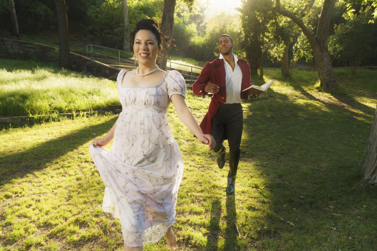 A woman and a man in period costumes run through a grassy clearing.