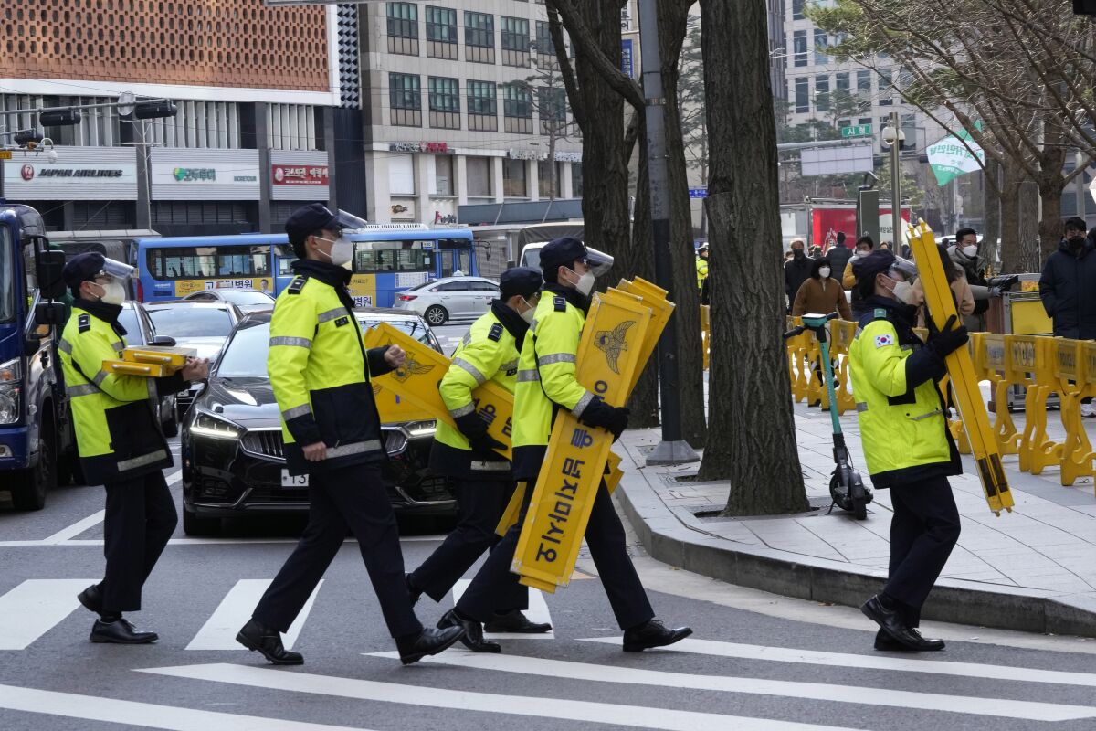 Police officers wearing face masks to help protect against the spread of the coronavirus carry barricades in Seoul, South Korea, Thursday, Dec. 2, 2021. South Korea broke its daily record for coronavirus infections for a second straight day on Thursday with more than 5,200 new cases, as pressure mounted on a health care system grappling with rising hospitalizations and deaths. (AP Photo/Ahn Young-joon)